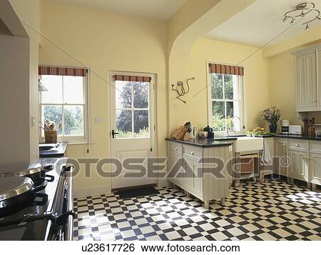Stock Photograph - Black+white vinyl flooring in pastel yellow country kitchen. Fotosearch