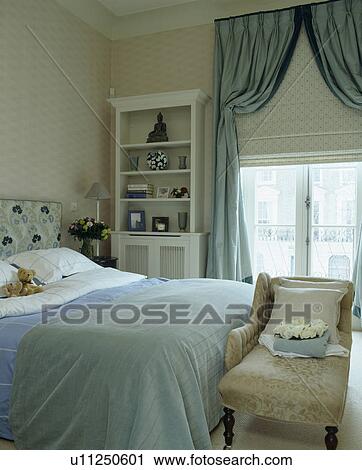 Stock Image - Blue bedcover on bed in townhouse bedroom with matching pale blue silk curtains on window with cream blind. Fotosearch