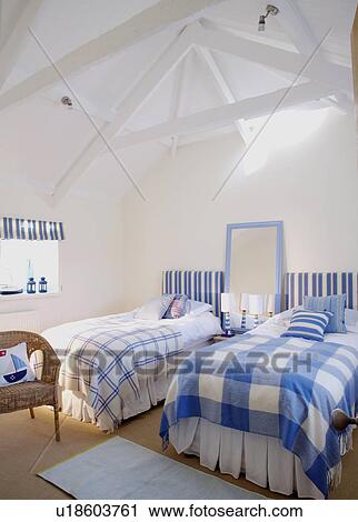 Stock Image - Blue checked blankets on twin beds in coastal loft conversion bedroom with white beamed apex ceiling. Fotosearch