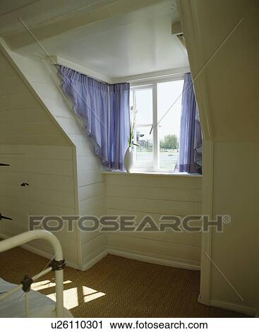 Stock Image - Blue curtains on portiere rods on awkwardly shaped dormer window. Fotosearch