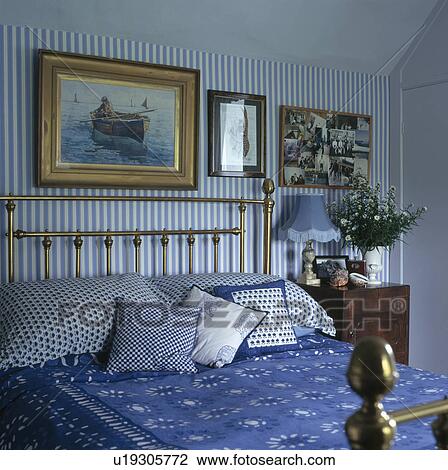 Stock Image - Blue striped wallpapder in bedroom with blue bedcover on brass bed. Fotosearch