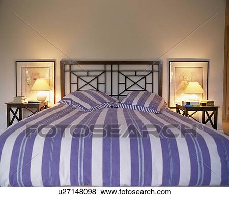 Blue+white striped bedlien on metal bed between lighted lamps on bedside tables View Large Photo Image Stock Photo - Blue+white striped bedlien on metal bed between lighted lamps on bedside tables. Fotosearch