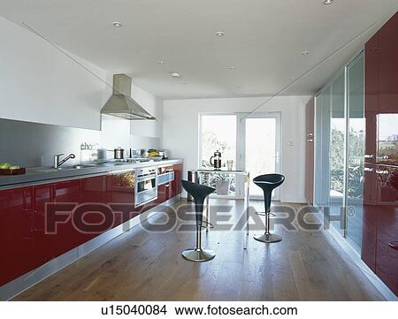 Bomba stools in large modern kitchen with red fitted units and wooden flooring View Large Photo Image Picture - Bomba stools in large modern kitchen with red fitted units and wooden flooring. Fotosearch