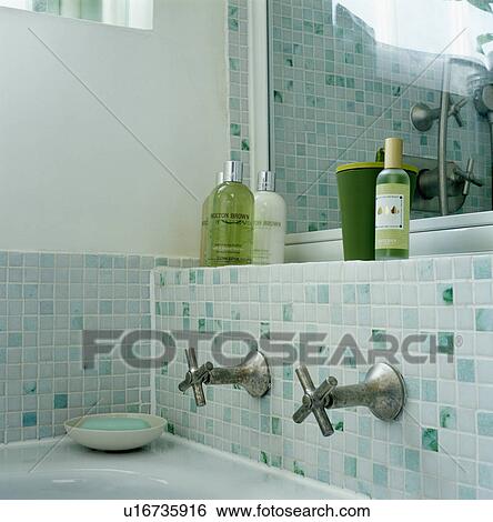 Bottles of bath oil on shelf above mosaic tiling and brushed steel taps View Large Photo Image Stock Photograph - Bottles of bath oil on shelf above mosaic tiling and brushed steel taps. Fotosearch