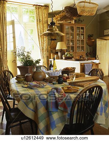 Stock Photo - Bottles of wine and loaf of bread on circular table with yellow+blue checked cloth in country kitchen. Fotosearch