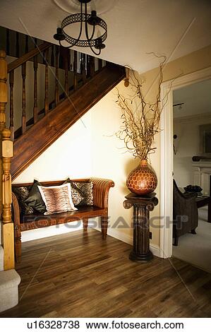 Branches in spherical pot on plinth beside wood settle with animalprint cushions in neutral hall with wooden flooring View Large Photo Image Stock Photo - Branches in spherical pot on plinth beside wood settle with animalprint cushions in neutral hall with wooden flooring. Fotosearch