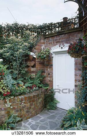Stock Photograph - Brick wall supporting raised bed beside white door in walled garden. Fotosearch