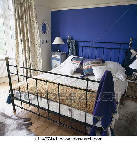Bright blue wall behind black metal bed in townhouse bedroom View Large Photo Image Stock Image - Bright blue wall behind black metal bed in townhouse bedroom. Fotosearch