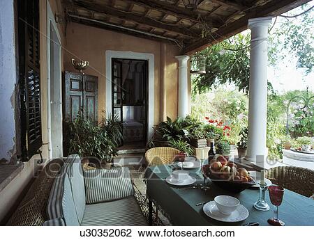 Stock Image - Chairs and table set for lunch on veranda of Mallorcan house with view of the garden. Fotosearch