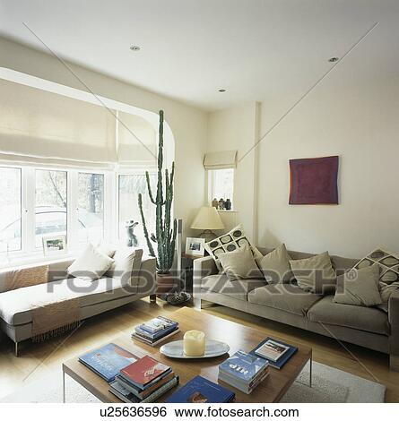 Chaiselongue below bay window with white blind in living room with beige sofa piled with cushions View Large Photo Image Stock Photograph - Chaiselongue below bay window with white blind in living room with beige sofa piled with cushions. Fotosearch