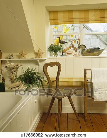Stock Image - Checked blind on window in attic bathroom with small wooden chair. Fotosearch