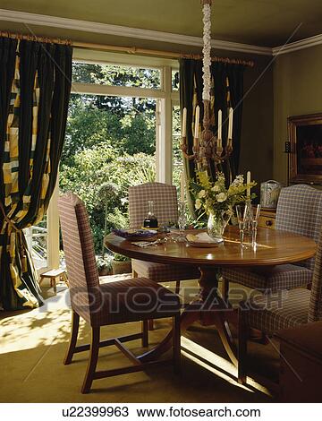 Checked upholstered chairs and antique circular table in dining room with patterned curtains at open French doors View Large Photo Image Stock Image - Checked upholstered chairs and antique circular table in dining room with patterned curtains at open French doors. Fotosearch