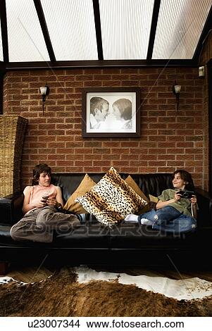Picture - Children sitting on black leather sofa in living room extension. Fotosearch