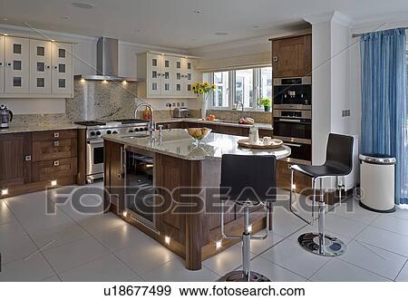 Stock Photo - Chrome and black stools at island unit in modern kitchen with lighting in kickplates and white ceramic tiled floor. Fotosearch