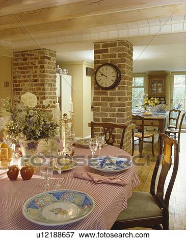 Circular antique clock on brick support wall in country dining room extension with pink cloth and place settings on table View Large Photo Image Stock Photo - Circular antique clock on brick support wall in country dining room extension with pink cloth and place settings on table. Fotosearch