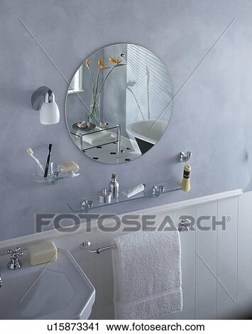 Circular unframed mirror and glass shelves above white towel on rail in grey bathroom View Large Photo Image Stock Image - Circular unframed mirror and glass shelves above white towel on rail in grey bathroom. Fotosearch