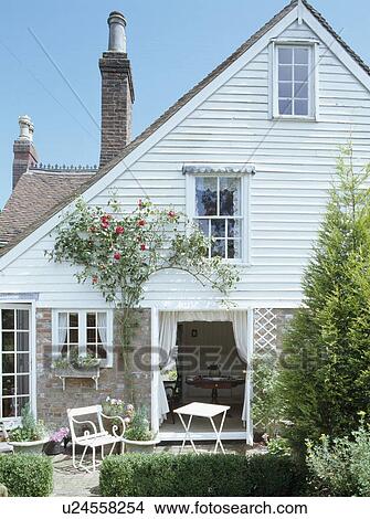 Clapboard cottage with bench and table on patio outside French doors and climbing rose over window View Large Photo Image Picture - Clapboard cottage with bench and table on patio outside French doors and climbing rose over window. Fotosearch