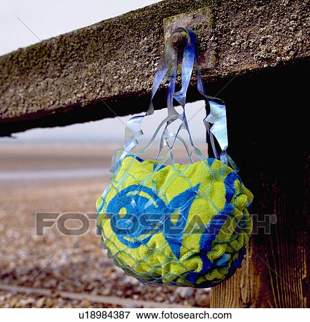 Stock Photo - Close-up of blue and green fish-patterned beach-towel in plastic net bag on break-water. Fotosearch