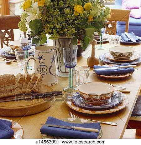 Stock Image - Close-up of blue and terracotta pottery bowls and plates on wooden dining table fresh flower arrangement. Fotosearch