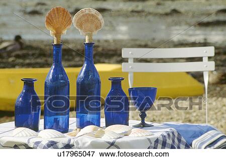 Stock Photo - Close-up of blue bottles with seashell stoppers on table on beach. Fotosearch