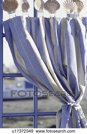 Stock Photo - Close-up of blue+white striped cotton curtain with seashell clips on window with view of harbour. Fotosearch