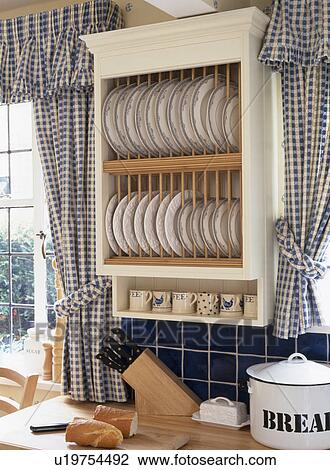 Close Up Of Cream Plate Rack And Blue Checked Curtains Stock Image