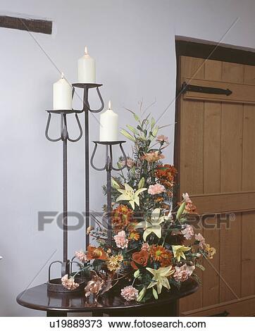 Close-up of formal floral arrangement on hall table with white candles in three tall cast-iron candlesticks View Large Photo Image Stock Image - Close-up of formal floral arrangement on hall table with white candles in three tall cast-iron candlesticks. Fotosearch