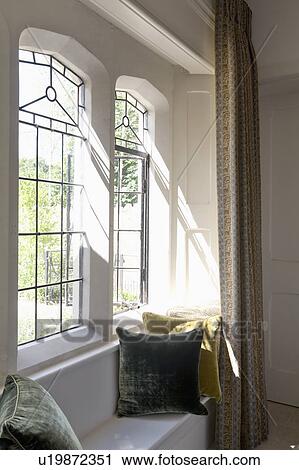 Stock Image - Close-up of green cushions on windowseat below leaded Arts+Crafts window. Fotosearch