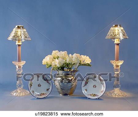 Stock Photography - Close-up of lighted candle lamps on either side of lustre-ware jug with cream freesias. Fotosearch