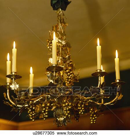 Stock Photography - Close-up of lighted candles on brass chandelier decorated with gilt grapes. Fotosearch