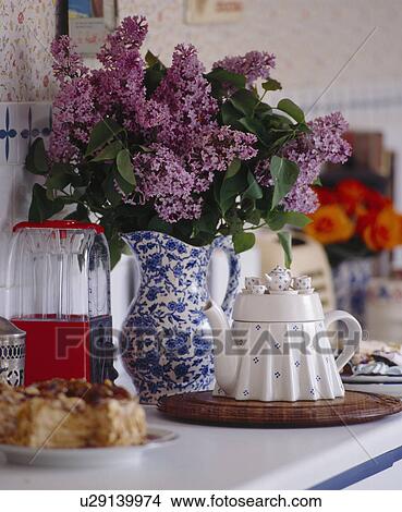 Picture - Close-up of mauve lilac in blue+white jug beside table-shaped teapot. Fotosearch