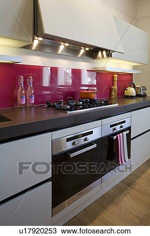 Stock Image - Close-up of Miele multi-function Pyrolytic ovens in modern kitchen with red glass splashbacks and cast resin worktop. Fotosearch