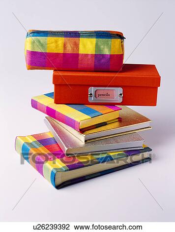 Stock Image - Close-up of multi-coloured checked pencil case on red box and pile of colourful notebooks. Fotosearch