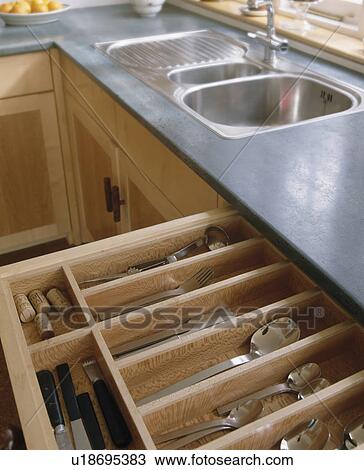 Stock Image - Close-up of open cutlery drawer below stainless steel sink in fitted unit with zinc worktop. Fotosearch