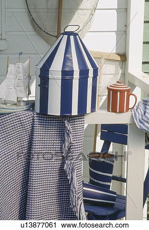 Stock Image - Close-up of painted blue+white striped tin box on white table. Fotosearch