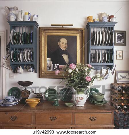 Stock Image - Close-up of picture between blue plate racks above pine chest-of-drawers. Fotosearch