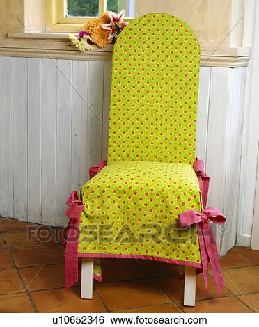 Stock Photograph - Close-up of pink-spotted lime-green loose-cover on dining chair against painted wooden dao. Fotosearch