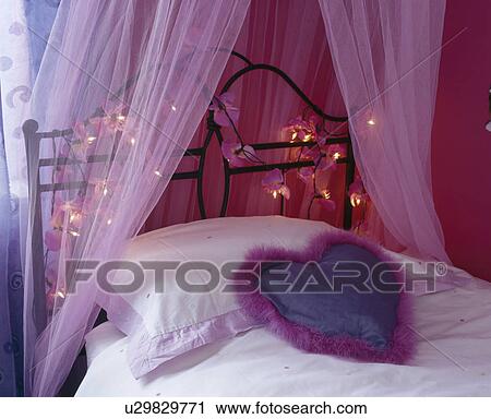 Stock Image - Close-up of pink voile curtains on iron bed with fairy lights . Fotosearch