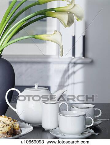 Stock Image - Close-up of platinum-edged white china teapot and matching cups and jug with white calla lilies. Fotosearch