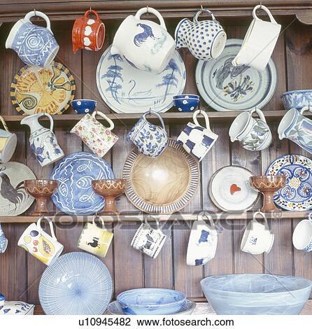 Stock Image - Close-up of pottery jugs and cups with plates on wooden dresser. Fotosearch