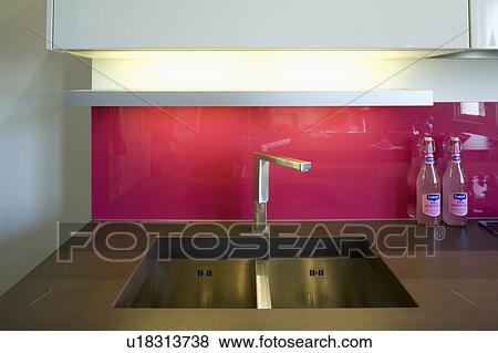 Stock Photo - Close-up of red glass splashback above stainless steel tap and sink. Fotosearch