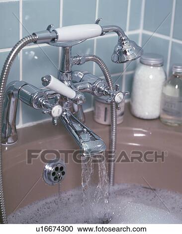 Stock Image - Close-up of shower head with taps pouring water into bath. Fotosearch