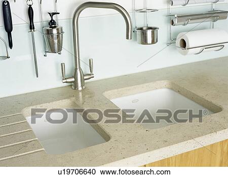 Stock Image - Close-up of stainless steel mixer tap above underset white ceramic double sinks. Fotosearch