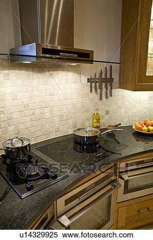 Stock Photography - Close-up of stainless steel pans on gas and halogen hobs. Fotosearch