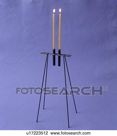Stock Image - Close-up of tall lighted candles in modern metal candlestick. Fotosearch