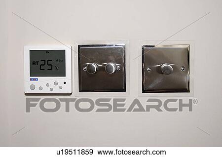 Stock Photo - Close-up of thermostat and stainless steel light switches. Fotosearch