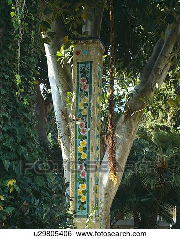 Stock Photograph - Close-up of tree with decorative floral tiled pillar. Fotosearch