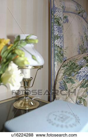 Close-up of Victorian style glass and brass lamp on table beside bed with blue floral headboard View Large Photo Image Stock Photo - Close-up of Victorian style glass and brass lamp on table beside bed with blue floral headboard. Fotosearch