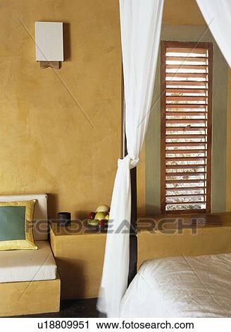 Stock Image - Close-up of white drapes in bedroom with rough yellow walls. Fotosearch