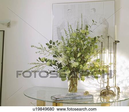 Close-up of white flowers and green leaves in glass vase on glass console table with tall candlestick View Large Photo Image Stock Image - Close-up of white flowers and green leaves in glass vase on glass console table with tall candlestick. Fotosearch
